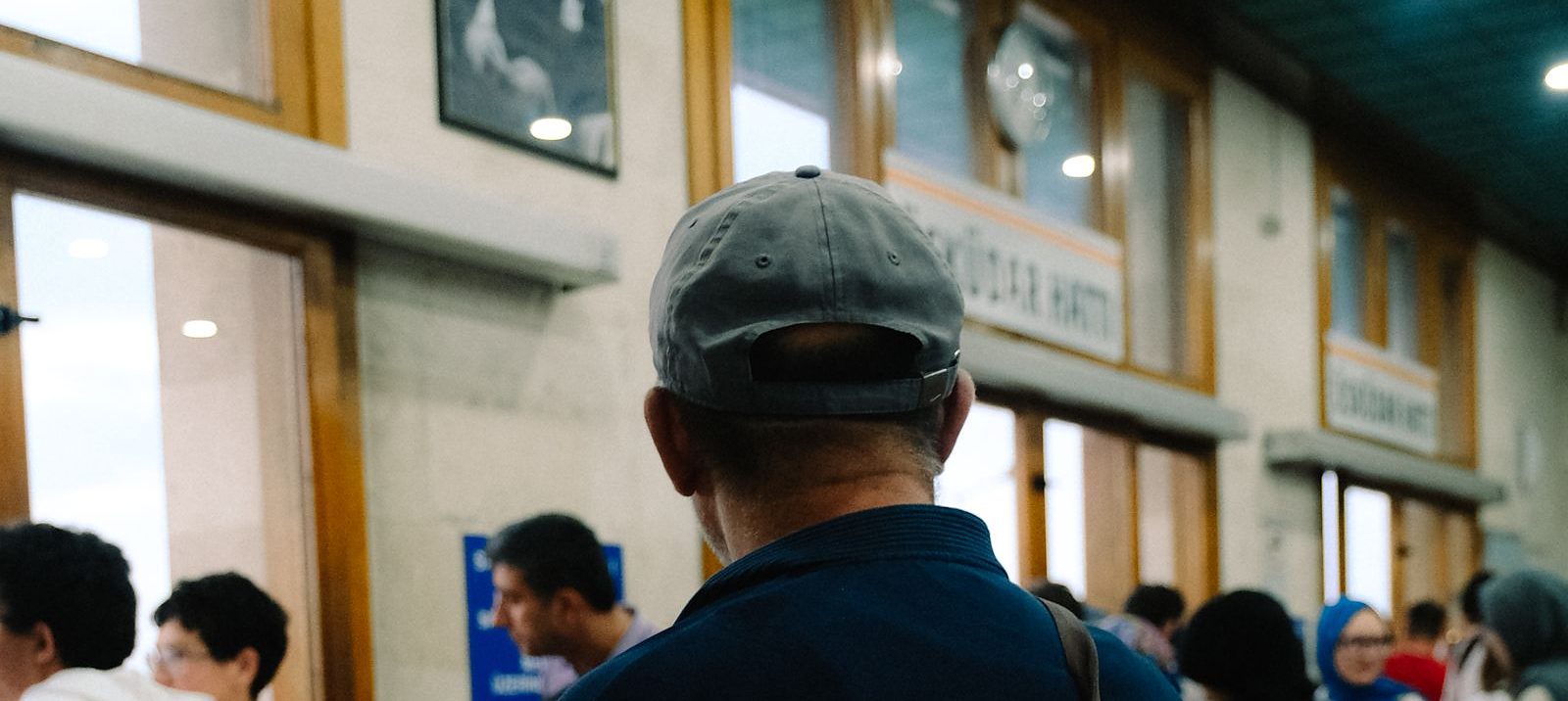 Un uomo di spalle in attesa nel salone di un ufficio pubblico, con gli sportelli in fondo