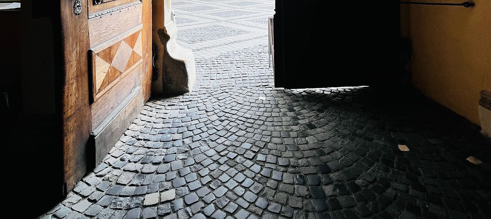 Il portone di un palazzo spalancato, visto dall&rsquo;androne verso la strada in luce