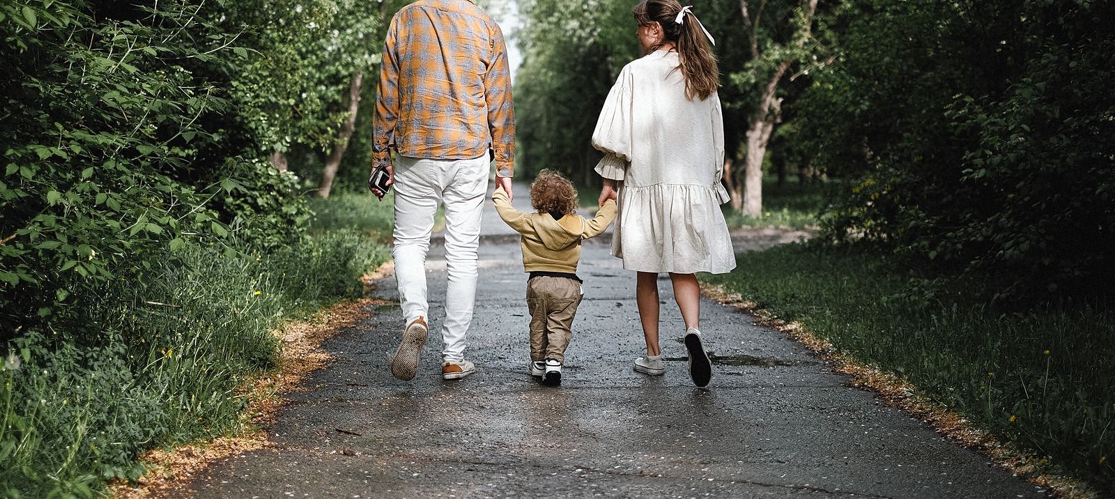 Una famiglia di tre che cammina di spalle lungo una strada
