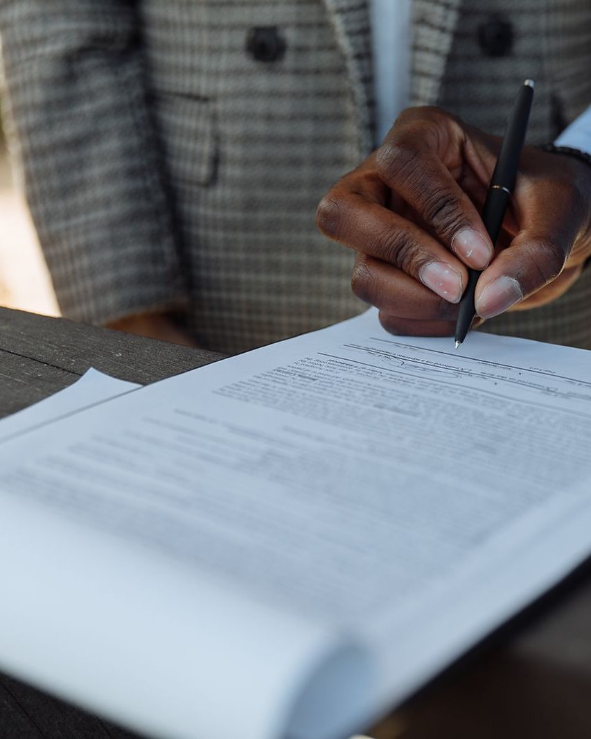 Una mano con la penna appoggiata sulla riga della firma, in fondo a un foglio
