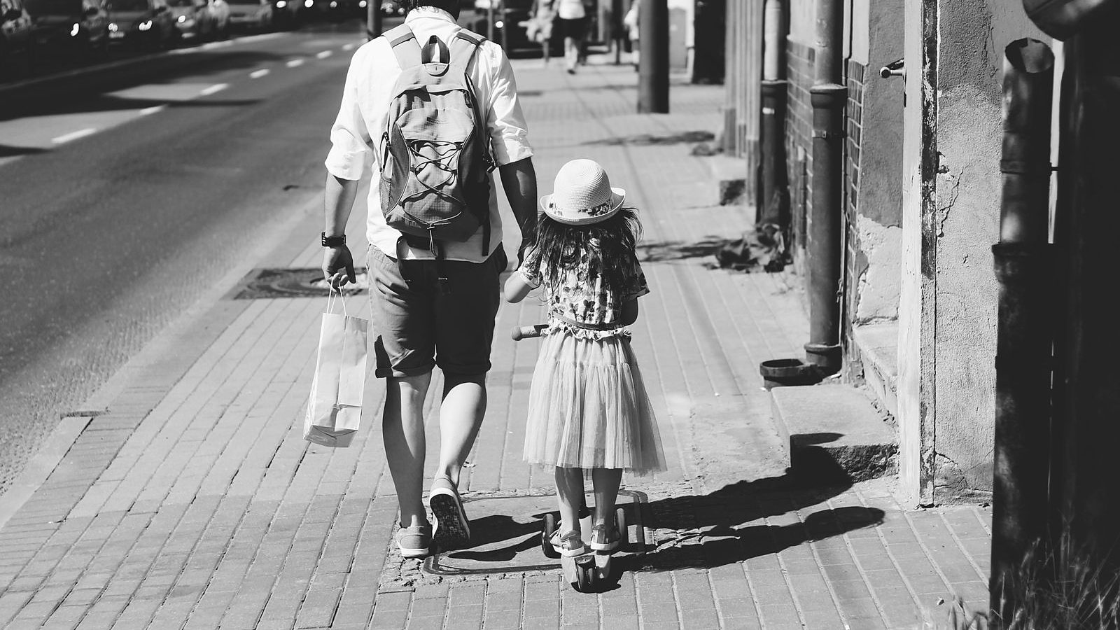 Un adulto che cammina di spalle tenendo per mano una bambina piccola